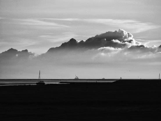 schwarz weiß Aufnahme vom Meer bei Ebbe mit großer Wolke am Himmel und kleinem Segelboot im Vordergrund