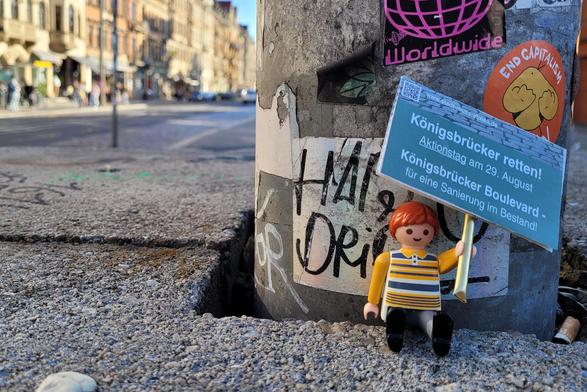 Die Playmobilfigur Kilian sitzt an der Kreuzung Alaunstraße / Königsbrücker Straße und hält ein Schild mit dem Aufruf zur Demo an der Schauburg zur Rettung der Königsbrücker Straße.