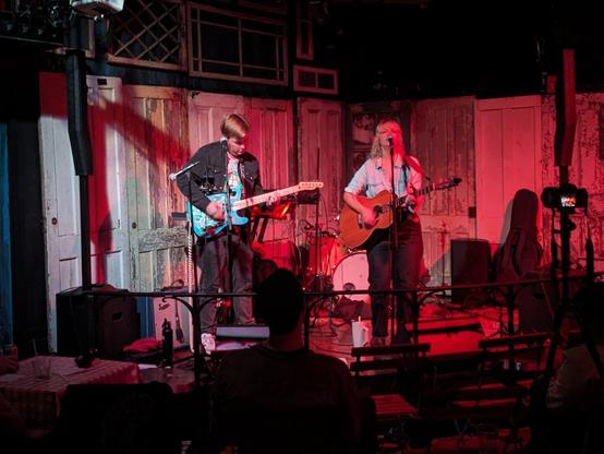 A photo of Sam Brown singing and playing guitar at Baker Falls. She is accompanied by a second guitarist.