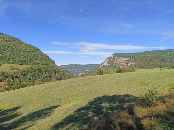 4 photos numériques couleur en format paysage, avec une vue panoramique d'une prairie bordée à gauche d'un relief boisé et à droite d'une falaise calcaire. Le ciel est bleu avec quelques nuages blancs.