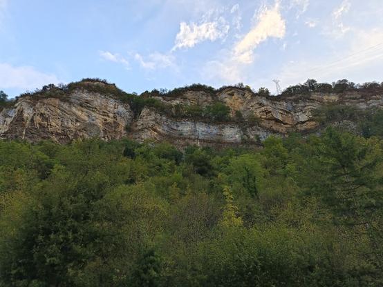 3 photos numériques couleur de différents formats, avec une vue en contre-plongée d'une falaise composée de différentes couches plus ou moins horizontales, au-dessus d'arbres. Le ciel est bleu avec quelques nuages blancs, avec une lumière un peu à contre-jour.