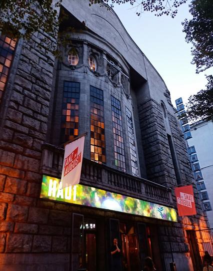 Die etwas düstere Fassade des theaters HAU 1, daran fahnen von TANZ IM AUGUST