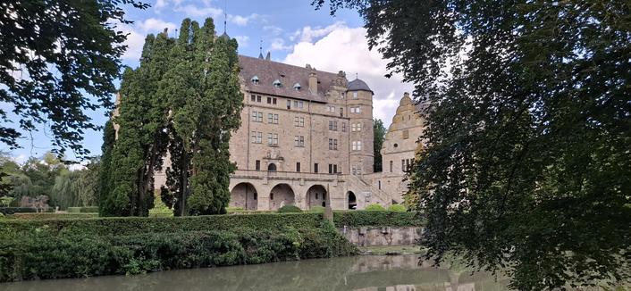 A photo of Neuenstein castle from the garden side. I the foreground a lake and trees.