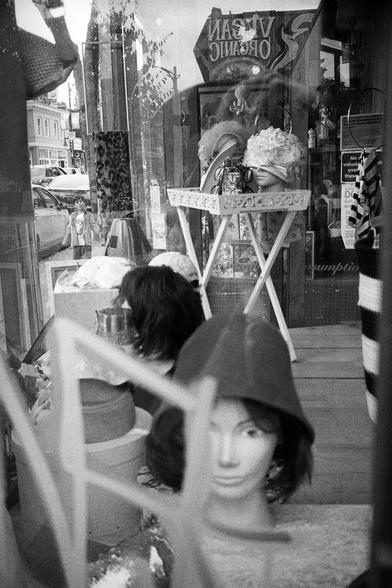 A boy strolls past the display of a thrift store. Various mannequin heads look on.