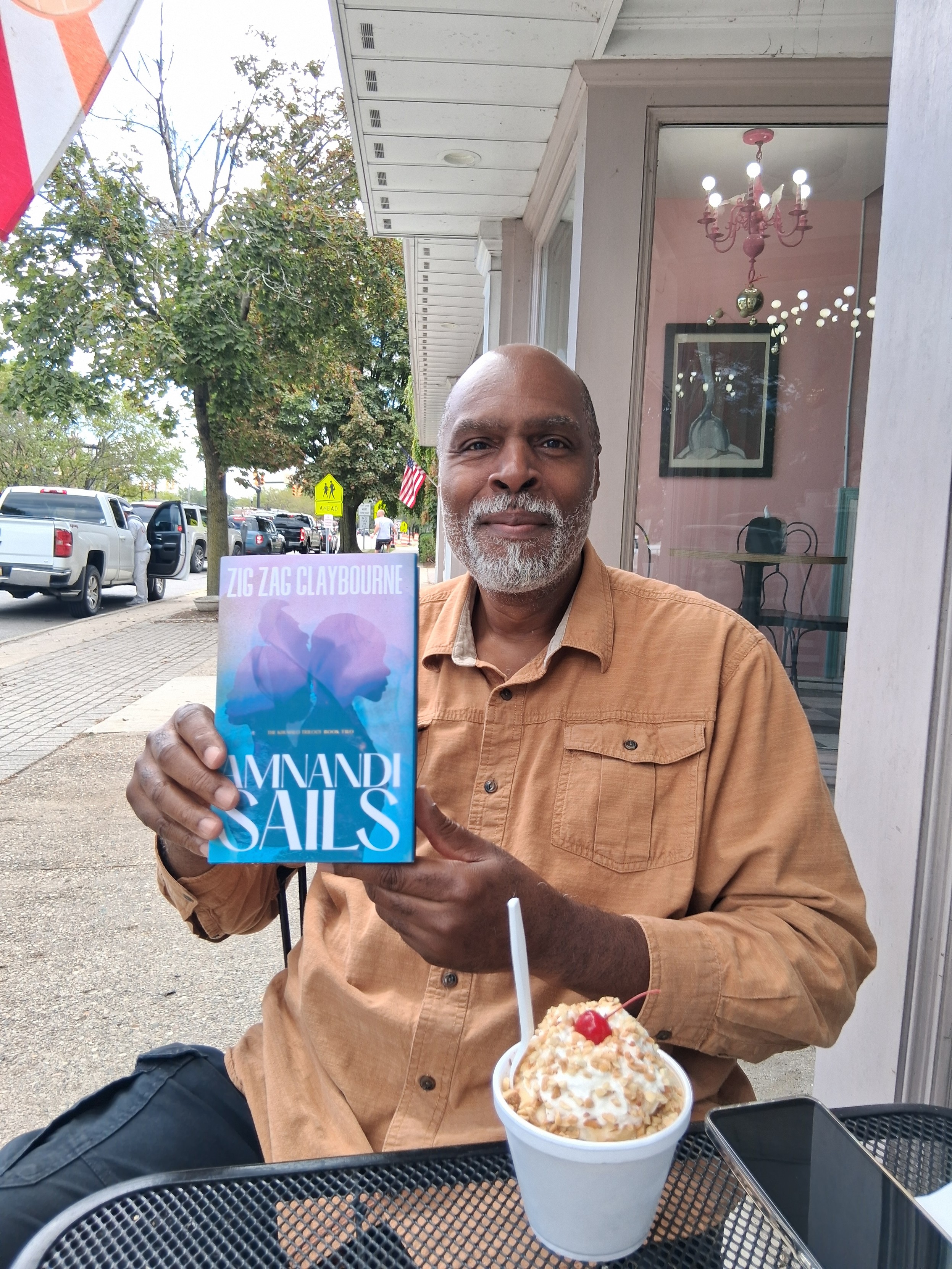 Smiling black guy with white goatee holding up a copy of his new book at a streetside cafe. A substantial sundae sits on the table between us. It has maybe a third of the nuts it should. The counter girl did not understand the meaning of 'sufficient nuts.' I blame the education system.