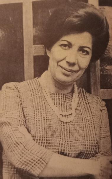 Retrato de Lupe Rivera Marín, destacada economista y activista mexicana, sonriendo y con los brazos cruzados, vestida con un blusón de cuadros y joyería en el cuello.