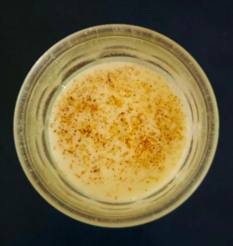 A drinking glass with a white liquid, kefir, and brown sprinkles, nutmeg, on top.