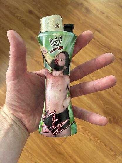 A novelty cigarette lighter the size of my outstretched hand palming it featuring the 1980s Wrestler "Hacksaw" Jim Duggan chambering his prized two-by-four over his shoulder