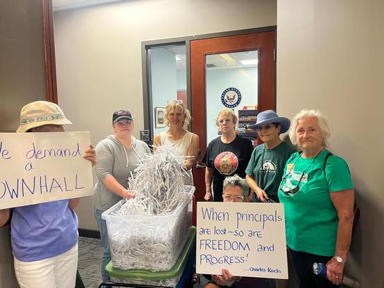 Volunteers holding signs and shredded pieces of paper in front of Rep. Simpson’s office
