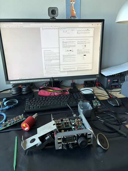 A desk with a keyboard, a monitor, an old amateur radio transceiver and lots of wiring