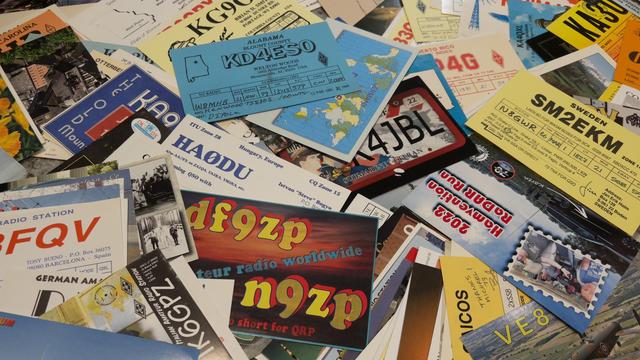 A collection of colorful amateur radio QSL cards are scattered, showcasing various designs and locations.