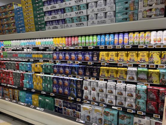 A supermarket shelf displaying a wide variety of canned and bottled beverages, including craft beers and cocktails. The products are arranged in colorful packages, with several brands visible, showcasing different flavors and styles.