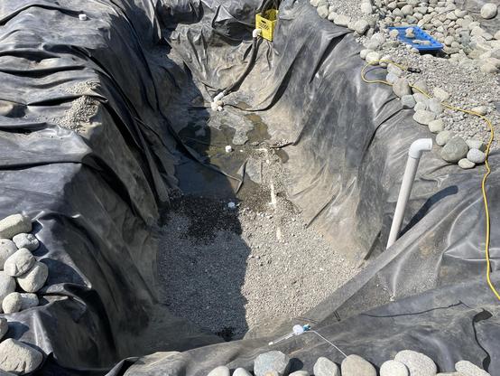 Along view of the newly emptied pond shows pebble spread over about 1/3 of the bottom of the hole covering some of the pipe for the sprayers