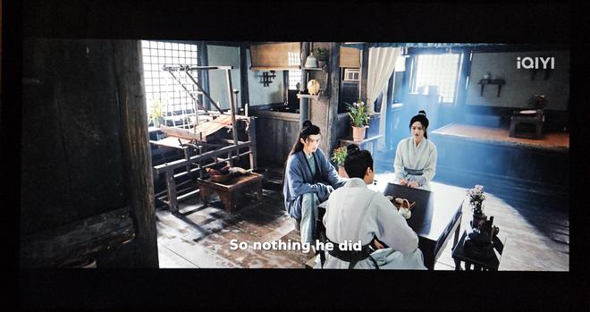 Beiming and Xueman talking to a person in a well kept and meticuosly clean room. The light from the window falls over a loom stringed with red warp.