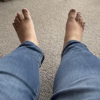 My bare feet, at the end of my legs with blue jeans, over textured carpet.