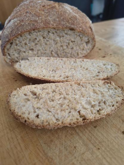 The loaf sitting on a bread board, with. slices cut, showing a wholemeal interior.