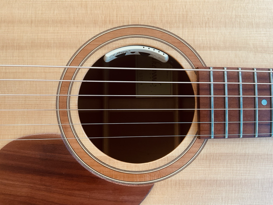 nahaufnahme von sechs saiten über dem schalloch einer akustikgitarre … rundherum  noch holz von hals, decke und pickguard