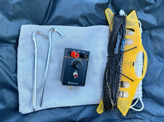 A wire antenna with its tuner, bag and some tent pegs
