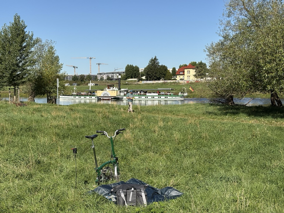 A meadow with a foldable bike and an amateur radio wire antenna in the front, the river Elbe with the steamboat Diesbar and some houses in the background