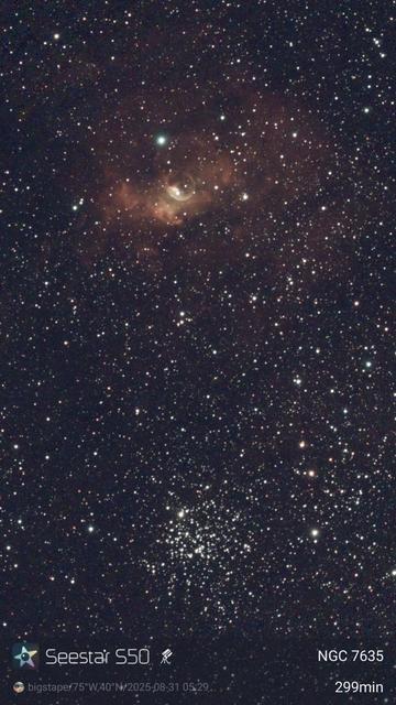 A cloud of glowing gas with a bubble in it above a loose ball of stars.