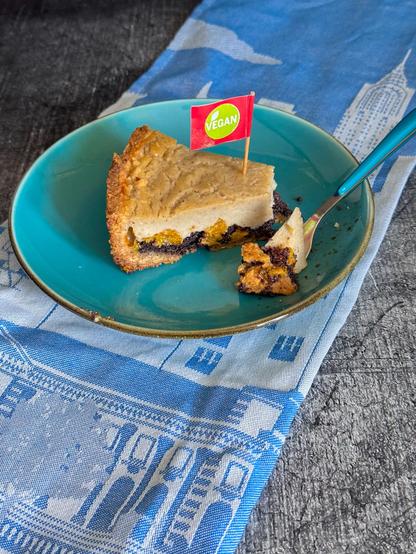 Ein Stück Käsemohnkuchen mit Mandarinen. Veganfahne steckt im Kuchen.