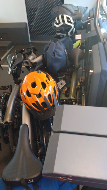 Fünf gefaltete Brompton-Falträder stehen im Veloabteil im Zug an hochgeklappten Notsitzen. Auf dem vordersten Brompton liegt ein orangener Velohelm.