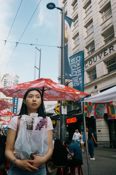A woman moves along the street with a plastic bag full of flowers.