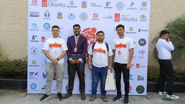Me (Center Right), Aaditya Singh (Center Left), standing in-between/alongside two other members of the community, in front of the UbuCon sponsors board.