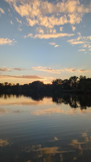 See und Wald im Dunkel, dahinter Himmel im Abendrot