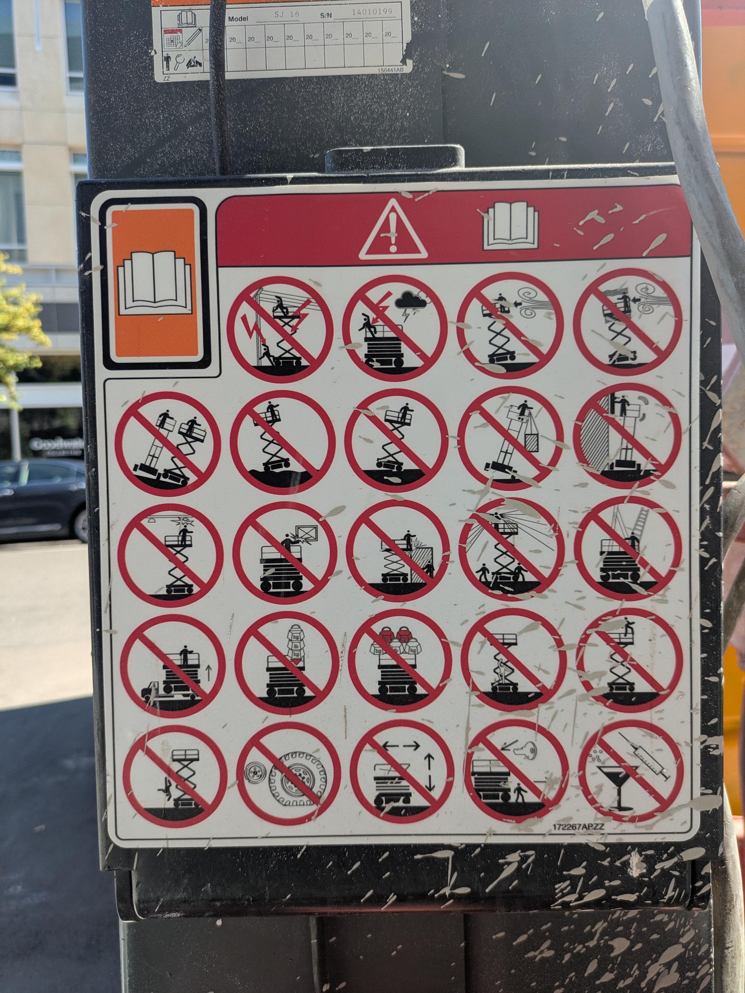 Closeup of a panel of 24 circular interdiction icons on the side of a scissor lift. They include: do not use during an electrical storm, do not tip either forward and back OR side to side, don't climb up the side, don't jump off, don't use as a crane, don't use when the tires are low, and don't use with a martini or hypodermic needle.