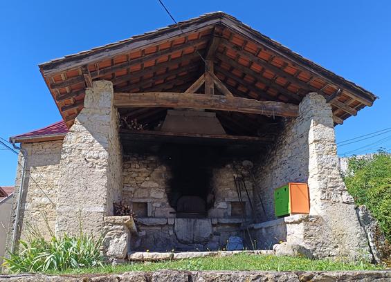 4 photos numériques couleur de différents formats, avec la vue en contre-plongée d'un four à pain en pierre surmonté d'un toit à 2 pans, qui est ouvert sur le village. Au fond, le four est noirci. A droite, un petit placard orange et vert qui est une cabane à livres. Le ciel est bleu.