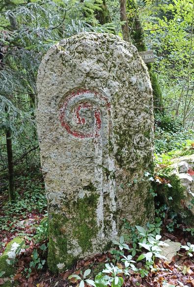 4 photos numériques couleur de différents formats, avec la vue rapprochée d'une grande borne en pierre, posée dans les bois près d'un chemin, sur laquelle est gravée la crosse de l'abbé du monastère proche dont dépendait ce lieu. Il reste des traces de peinture rouge sur la crosse.