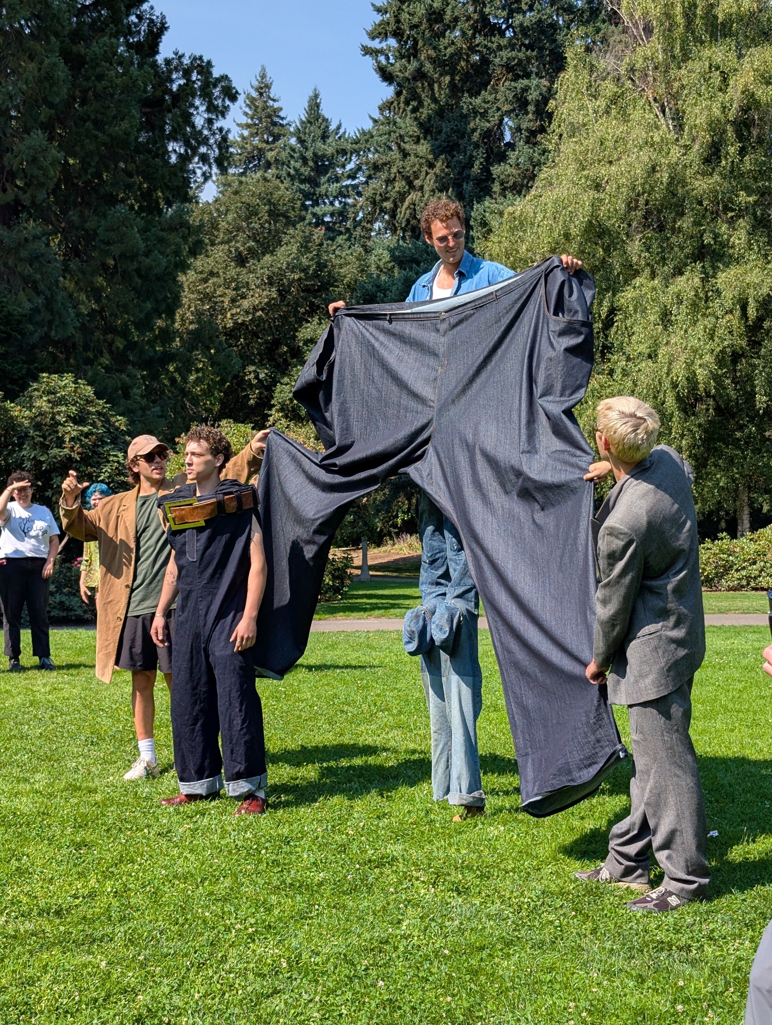 A guy on stilts holding a pair or large jeans surrounded by his friends.