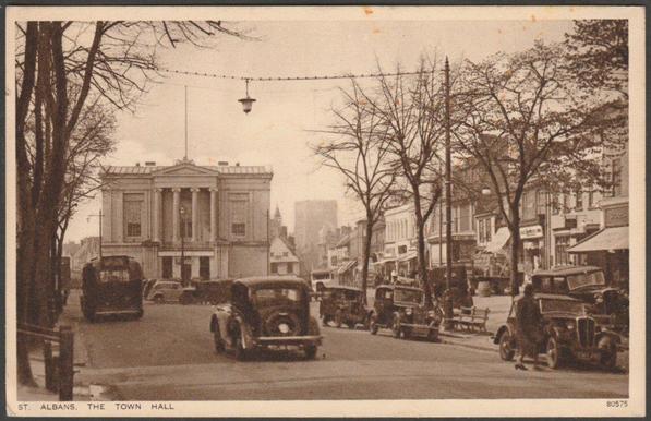 Printed sepia postcard showing a view of the Town Hall and surrounding shops at St Albans in Hertfordshire.

Published by Photochrom Co Ltd, Royal Tunbridge Wells, No 80575, c.1940s.

Postally unused.

Very good condition, with very slight corner bumps.