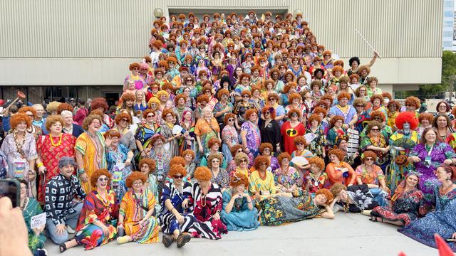 A large group of people dressed in kaftans, many with red curly wigs and sunglasses, gathered on and overflowing a large set of steps