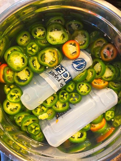 A metal bowl filled with sliced jalapenos in water with ice packs.
