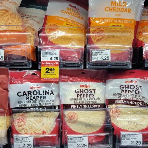 Packages of shredded cheese in a supermarket: mild cheddar, Carolina Reaper, Ghost Pepper
