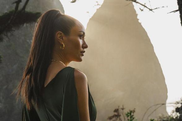 Model wearing earring and necklace with mountain in background.