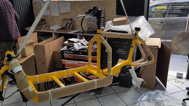 Vélocargo Bullitt jaune en cours d'assemblage suspendu par des sangles dans un atelier