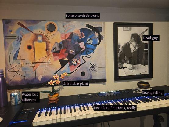 Funny labels on different studio objects. Painting: 'someone else's work.' Photo of Shostakovich: 'dead guy.' LEGO orchid: 'unkillable plant.' Singing bowl: 'bowl go ding.' Seltzer: 'water but different.' Piano keyboard: 'just a lot of buttons, really.'