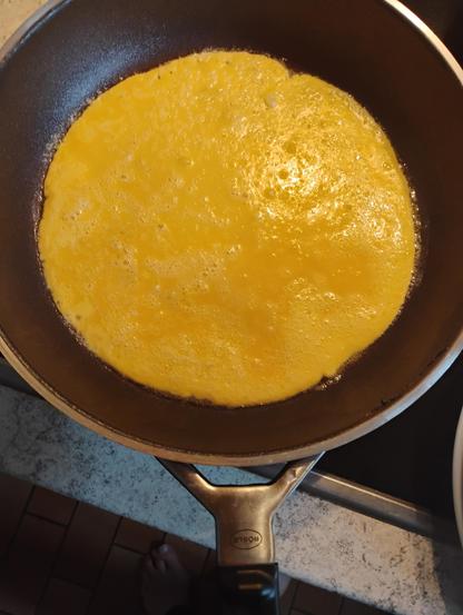 Ein goldgelber Pfannkuchen in einer Bratpfanne. An den Rändern kleine Bläschen von Butterschaum.