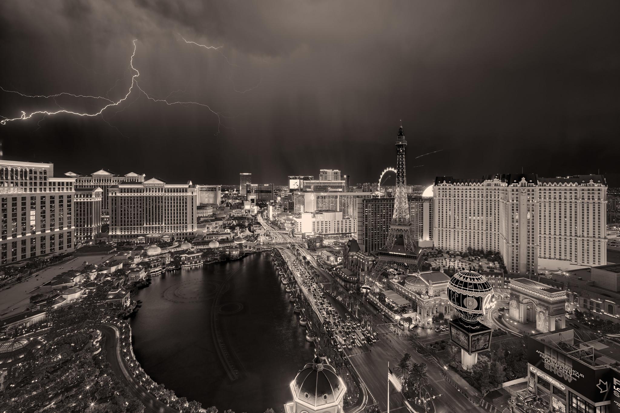 The Las Vegas Strip during a thunderstorm, with lightning bolts in background. There's a fake Eiffel Tower, a ferris wheel, a creepy sphere, and an inappropriately large fountain. Best viewed from a distance.