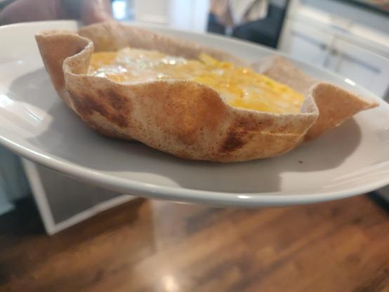 a plate with a tortilla and egg on it, from the side.

The tortilla edges are turned up, and you can see browned/blackened edges on the underside.