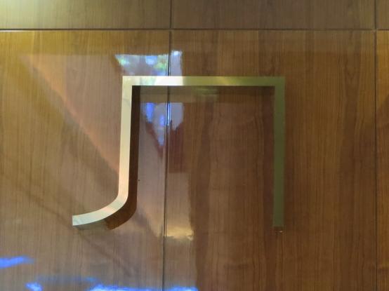 Латунная буква Л на стене, покрытой деревянными панелями. // A brass letter Л (Cyrillic L) on a wood paneled wall.