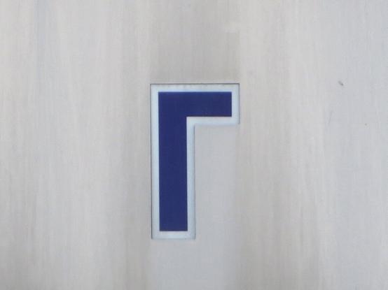 Синяя буква Г с белой обводкой, стикер на фасаде общественного здания. // A blue letter Г (Cyrillic G) with a white outline, a sticker on the facade of a public building.