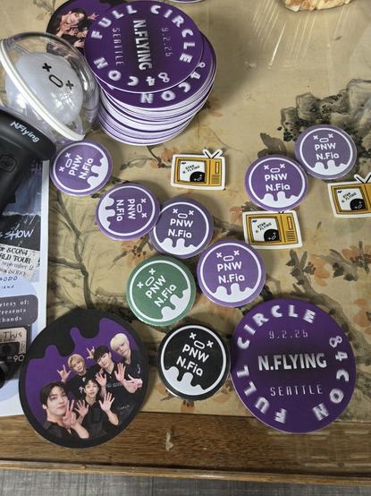 Merchandise items on a table. Some are buttons that say PNW N.Fia, some are drink coasters, some are stickers.