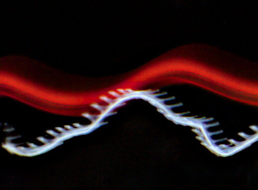 A light painting photograph showing the motion of a passing car at night. A red wavy light trail flows across the top, while a white zigzagging line with evenly spaced breaks runs below it, revealing the pulsing frequency of the car’s LED lights against the dark background.