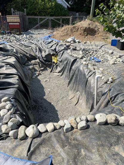The pool pond has gravel in the bottom now. There is a line of rocks along the edge closest to the camera before it goes down into the hole.