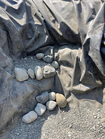 a closeup of the bottom stair with four rocks along the bottom of the pond edge and four more along the stair edge. The pond liber has lots of creases and edges as it has not been pulled tight.