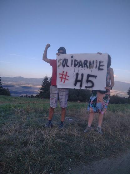 Dwie osoby trzymające baner. Tekst na banerze: Solidarnie #H5